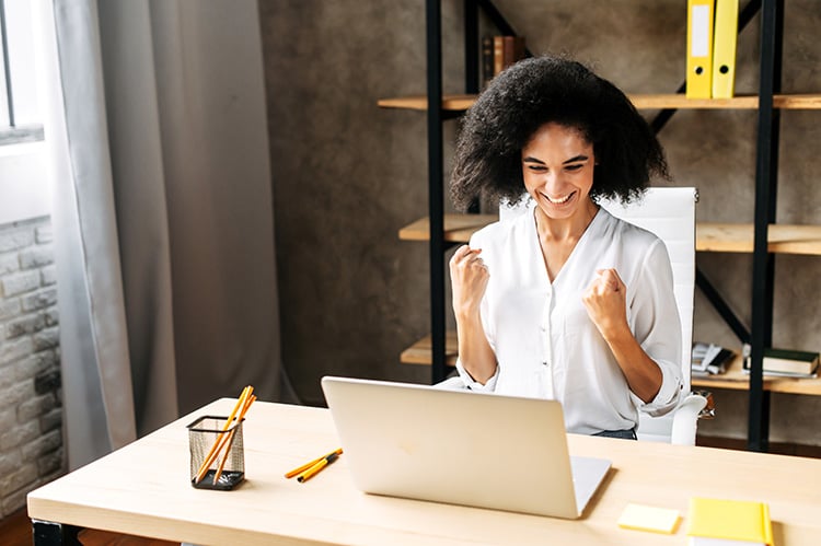 Smiling businesswoman pumps her fists in excitement while looking at her laptop in an office