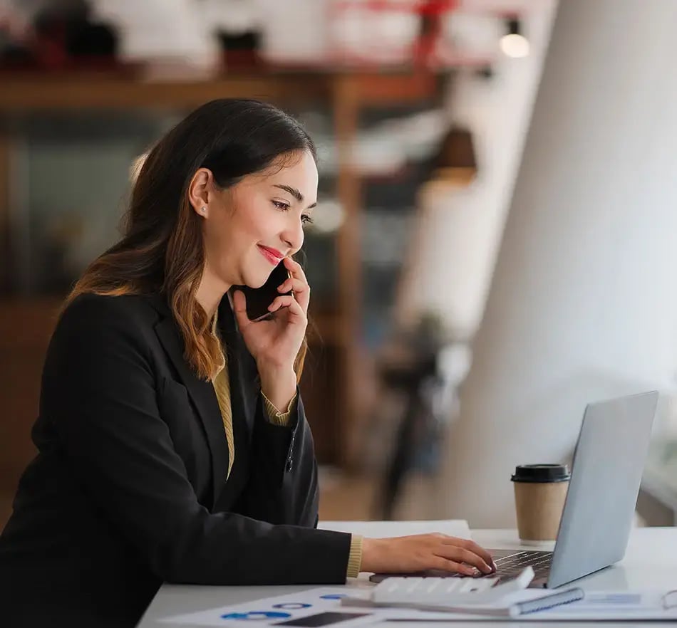 Lady on laptop with a coffee and a cell phone to her ear