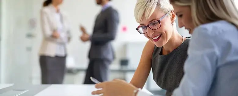 Two people reviewing documents with charts and other ERP resources at an office table, with two coworkers in the background
