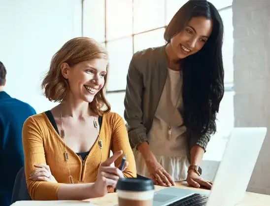 Two smiling businesswomen look at a laptop screen