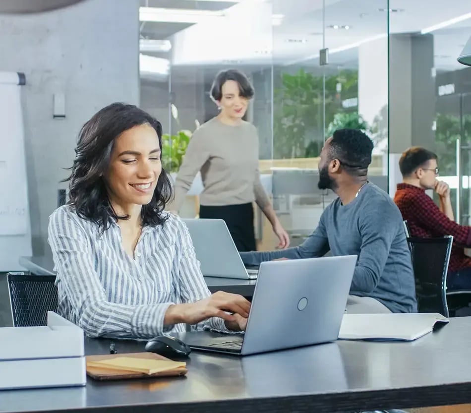 Lady in office setting with co-workers, using a laptop